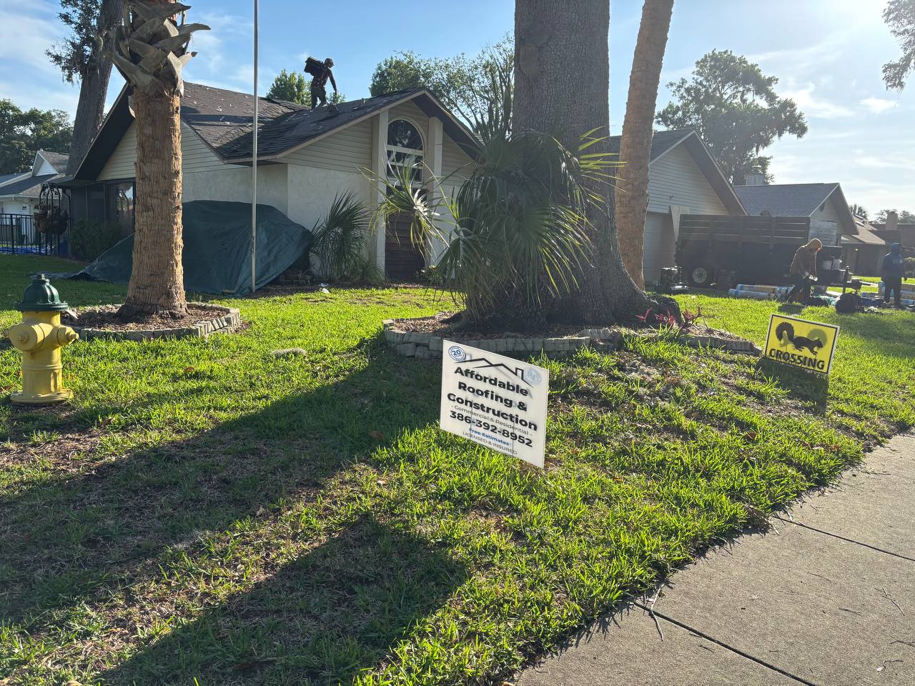 Roofing crew member working on roof with yard sign in foreground — Port Orange FL roof replacement in action